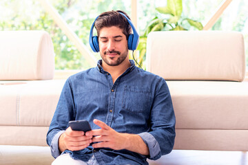 A man is relaxing on the sofa at home with headphones and mobile phone and listening to music