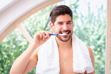 A stubble faced man standing in the bathroom at home and brushing his teeth