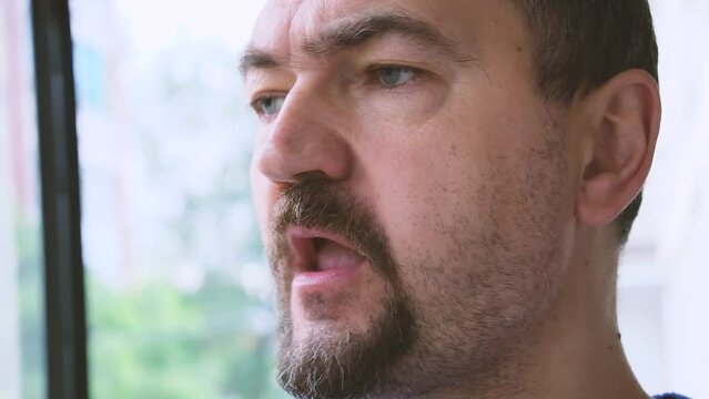 Unshaven man eating apples while looking out the window