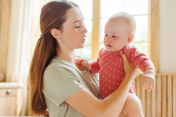 Beautiful young mother holding her little baby comforting her in living room at home