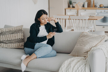 Modern woman uses mobile apps at home, leisurely browsing on couch. Focused on social networks, messaging, news, and online shopping.