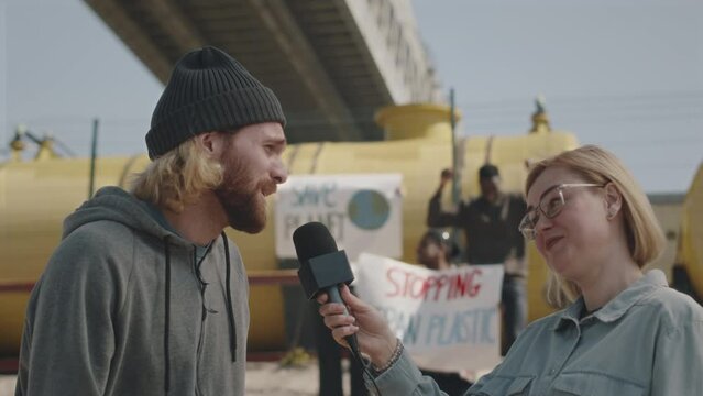 DescriptionYoung male environmental activist giving interview to TV journalist during protest against pollution, people with posters in background