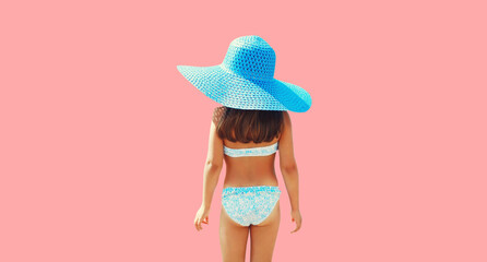Summer vacation, rear view little girl standing in straw hat isolated on pink background