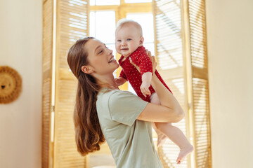 Mother holding her cute little baby in living room at home. Babysitter taking care of infant