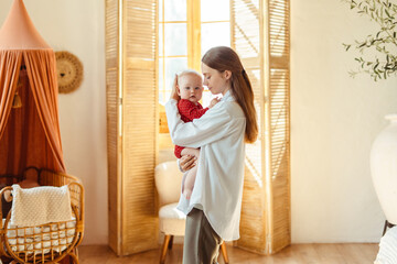 Beautiful young mother with closed eyes holding little baby in living room at home