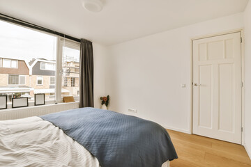 a bedroom with white walls and hardwood flooring the room has a large window that looks out onto the street