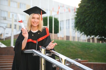 Portrait enthusiastic female college student graduate in cap and gown celebrating, holding diploma.