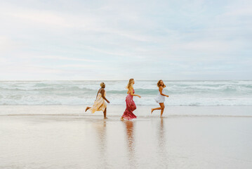 multiracial group of three young women running along the shore on the beach. friends enjoying their...