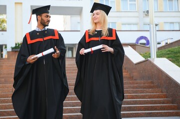 education, graduation and people concept - happy international students in mortar boards and bachelor gowns.