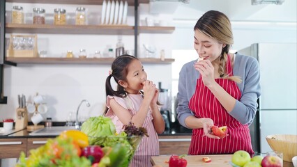 Young asian mother and little daughter enjoy eating apples in kitchen room at home. Eating fruit for health care. Happy asian family, Healthy food concept - obrazy, fototapety, plakaty