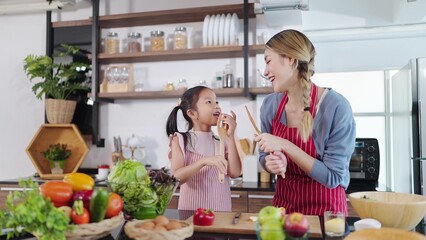 Happy asian mother and little daughter holding kitchen equipment on hands enjoy singing and dancing together in kitchen room at home. Single mom concept, Happy asian family