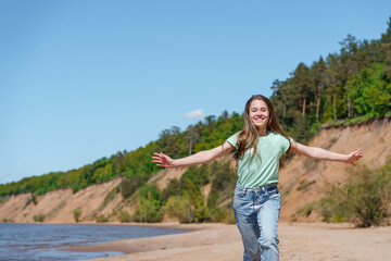 A teenage girl with long hair and jeans runs and frolics on the beach