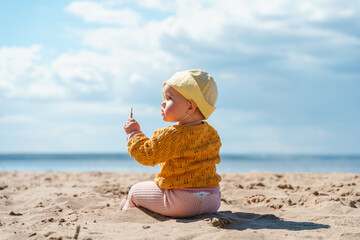 Fototapeta na wymiar Cute baby toddler playing with sand on the beach in the cold season