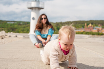 Mom and daughter - a little girl baby toddler - sit on the background of a lighthouse in summer
