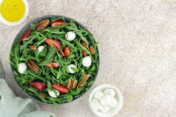 Green salad with strawberries, mozzarella balls, arugula and pecans on pink background. Top view. Copy space.