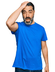 Fototapeta premium Middle aged man with beard wearing casual blue t shirt surprised with hand on head for mistake, remember error. forgot, bad memory concept.