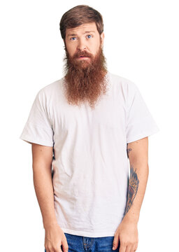Handsome young red head man with long beard wearing casual white tshirt relaxed with serious expression on face. simple and natural looking at the camera.