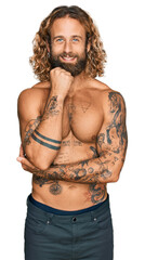 Fototapeta premium Handsome man with beard and long hair standing shirtless showing tattoos with hand on chin thinking about question, pensive expression. smiling and thoughtful face. doubt concept.