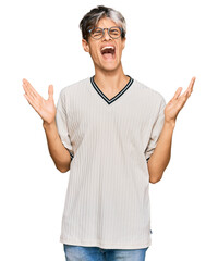 Naklejka premium Young hispanic man wearing casual clothes and glasses celebrating mad and crazy for success with arms raised and closed eyes screaming excited. winner concept