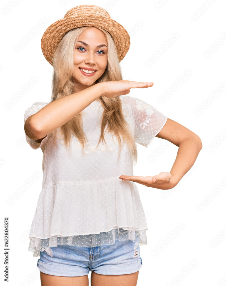 Sticker Young blonde girl wearing summer hat gesturing with hands showing big and large size sign, measure symbol. smiling looking at the camera. measuring concept.