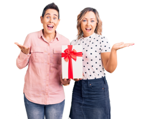 Couple of women holding gift celebrating victory with happy smile and winner expression with raised hands