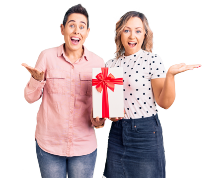 Couple of women holding gift celebrating victory with happy smile and winner expression with raised hands