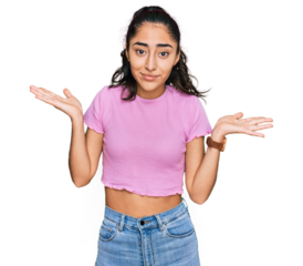 Hispanic teenager girl with dental braces wearing casual clothes clueless and confused expression with arms and hands raised. doubt concept.
