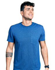 Fototapeta premium Young hispanic man wearing casual t shirt looking away to side with smile on face, natural expression. laughing confident.