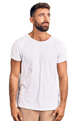 Young hispanic man wearing casual white tshirt smiling looking to the side and staring away thinking.