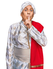 Senior hispanic man wearing tradition sherwani saree clothes asking to be quiet with finger on lips. silence and secret concept.