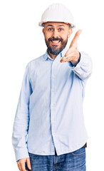Young handsome man wearing architect hardhat smiling friendly offering handshake as greeting and welcoming. successful business.