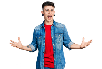 Young caucasian boy with ears dilation wearing casual denim jacket crazy and mad shouting and yelling with aggressive expression and arms raised. frustration concept.