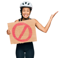 Beautiful hispanic woman wearing bike helmet and holding stop banner celebrating victory with happy smile and winner expression with raised hands
