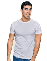 Obraz premium Handsome hispanic man wearing casual white t shirt looking away to side with smile on face, natural expression. laughing confident.