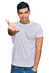 Naklejka premium Handsome hispanic man wearing casual white t shirt smiling friendly offering handshake as greeting and welcoming. successful business.