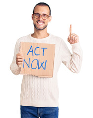 Young handsome man holding act now banner surprised with an idea or question pointing finger with happy face, number one