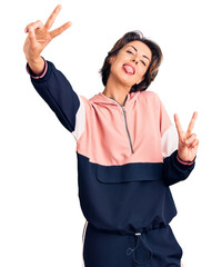 Young beautiful woman wearing sportswear smiling with tongue out showing fingers of both hands...