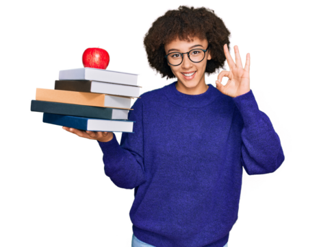 Young hispanic girl wearing glasses holding books and red apple doing ok sign with fingers, smiling friendly gesturing excellent symbol