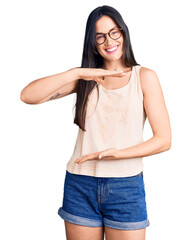 Young beautiful caucasian woman wearing casual clothes and glasses gesturing with hands showing big and large size sign, measure symbol. smiling looking at the camera. measuring concept.