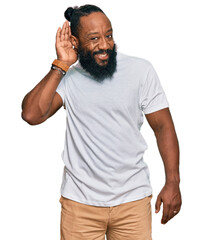 Young african american man wearing casual white tshirt smiling with hand over ear listening an hearing to rumor or gossip. deafness concept.