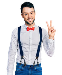 Hispanic man with beard wearing hipster look with bow tie and suspenders smiling with happy face...