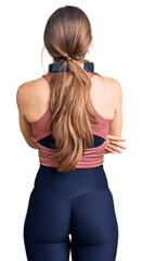 Beautiful caucasian young woman wearing gym clothes and using headphones standing backwards looking away with crossed arms