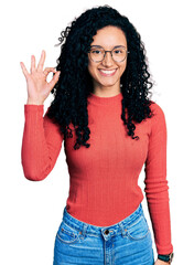 Young hispanic woman with curly hair wearing glasses smiling positive doing ok sign with hand and fingers. successful expression.