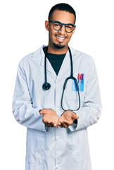 Young african american man wearing doctor uniform and stethoscope smiling with hands palms together receiving or giving gesture. hold and protection