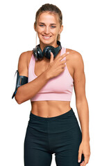 Young blonde woman wearing gym clothes and using headphones cheerful with a smile of face pointing with hand and finger up to the side with happy and natural expression on face
