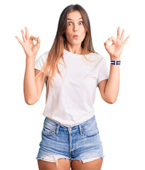 Beautiful caucasian woman wearing casual white tshirt looking surprised and shocked doing ok approval symbol with fingers. crazy expression