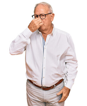 Senior caucasian man wearing business shirt and glasses smelling something stinky and disgusting, intolerable smell, holding breath with fingers on nose. bad smell