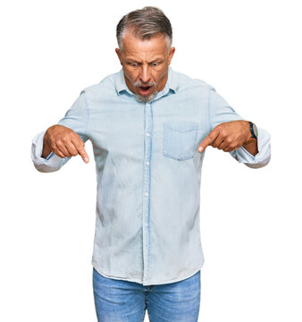 Middle age grey-haired man wearing casual clothes pointing down with fingers showing advertisement, surprised face and open mouth