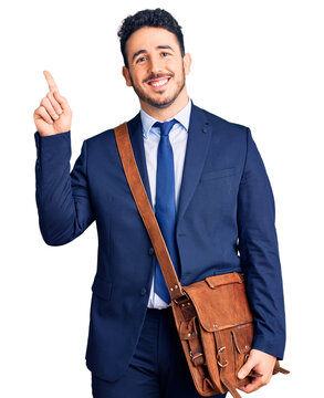 Young hispanic man wearing suit and leather bag surprised with an idea or question pointing finger with happy face, number one