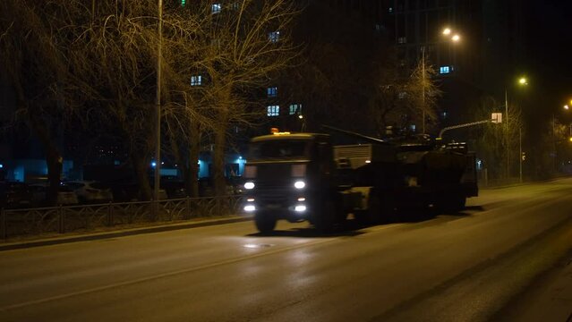 Night road with military tank riding on truck. Concept. Night transportation of military tank by truck. Military tank is transported by truck along empty night street